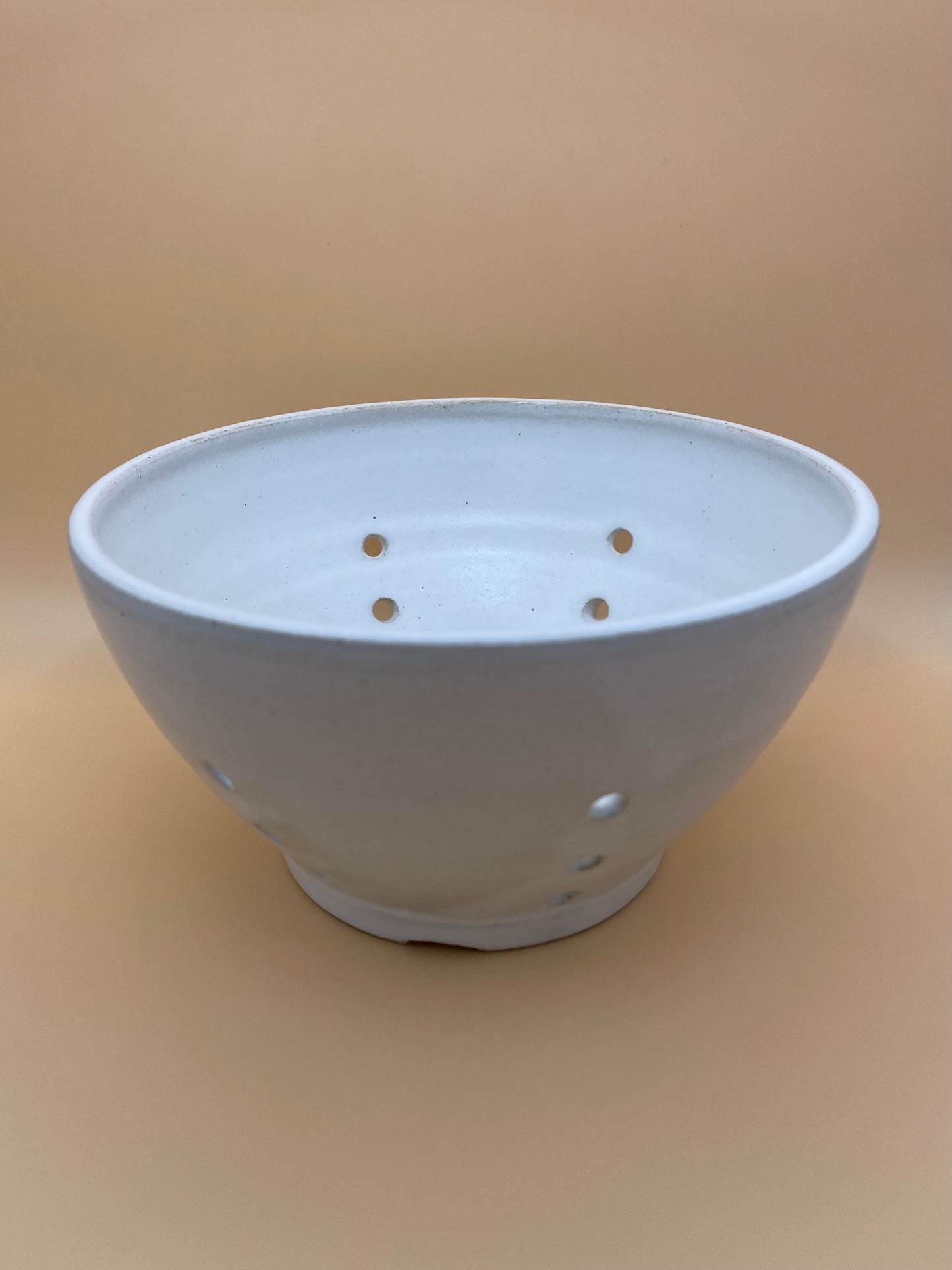 Angled side and inside view of handmade ceramic berry bowl with white glaze and drainage holes