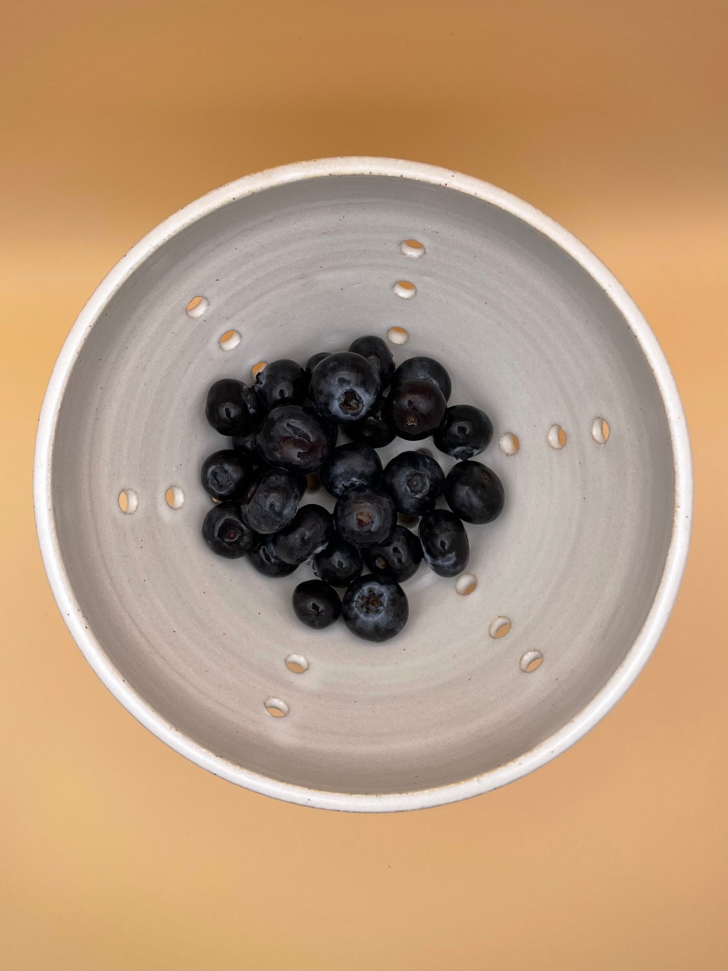 Overhead view of white ceramic berry bowl with blueberries and visible drainage holes