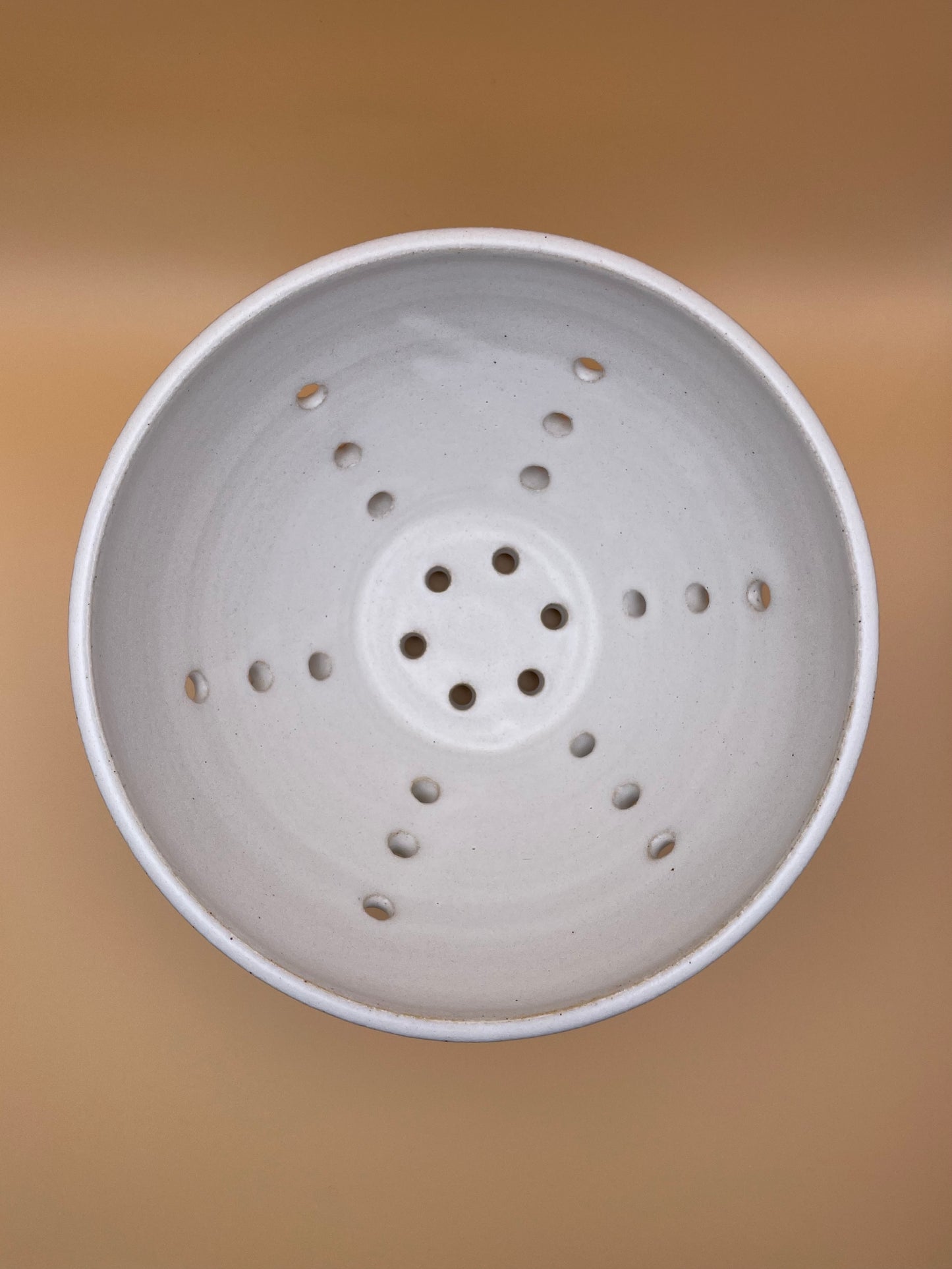 Top view of handmade white ceramic berry bowl showing interior glaze and drainage holes
