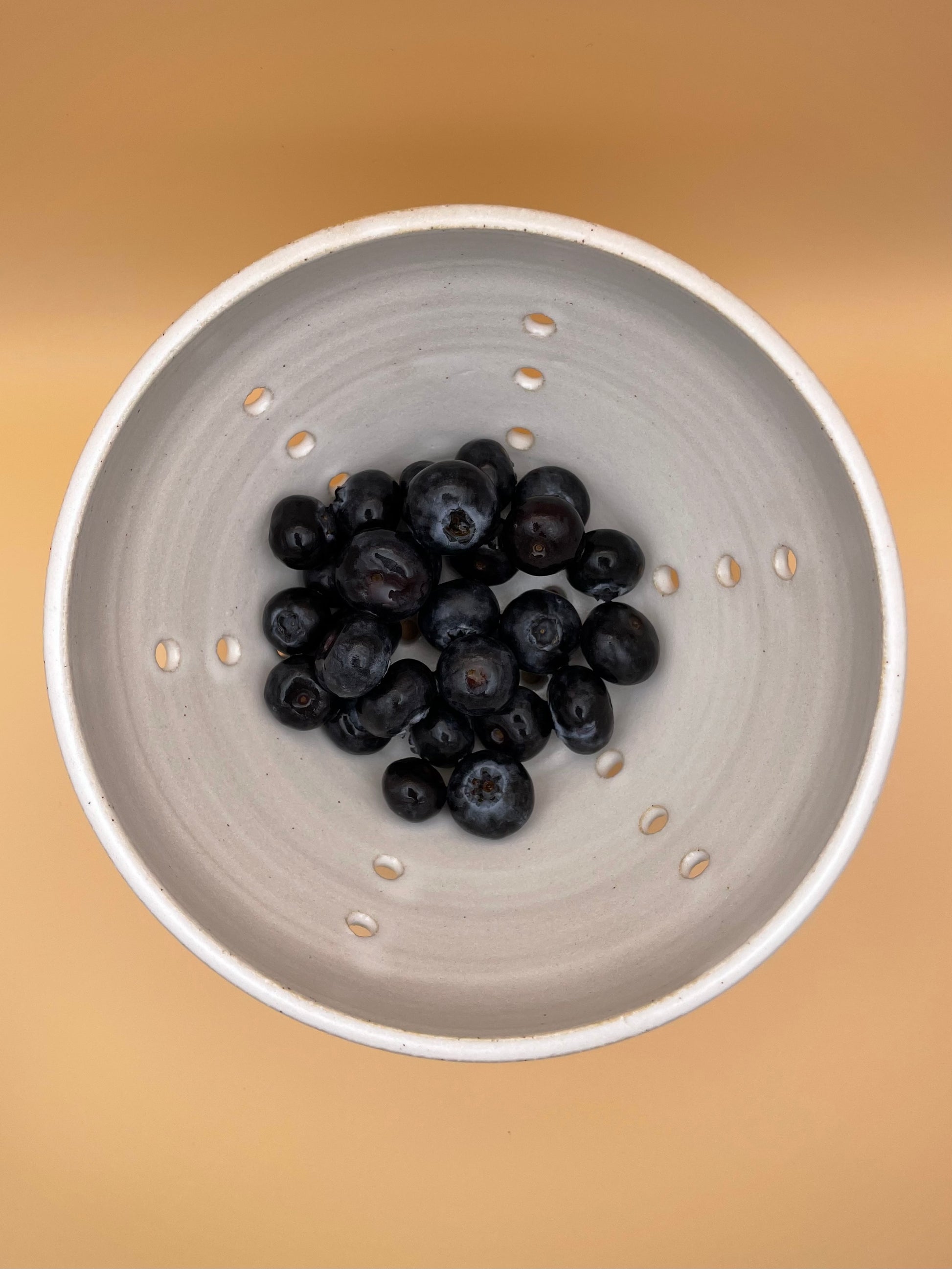 Overhead view of white ceramic berry bowl with blueberries and visible drainage holes
