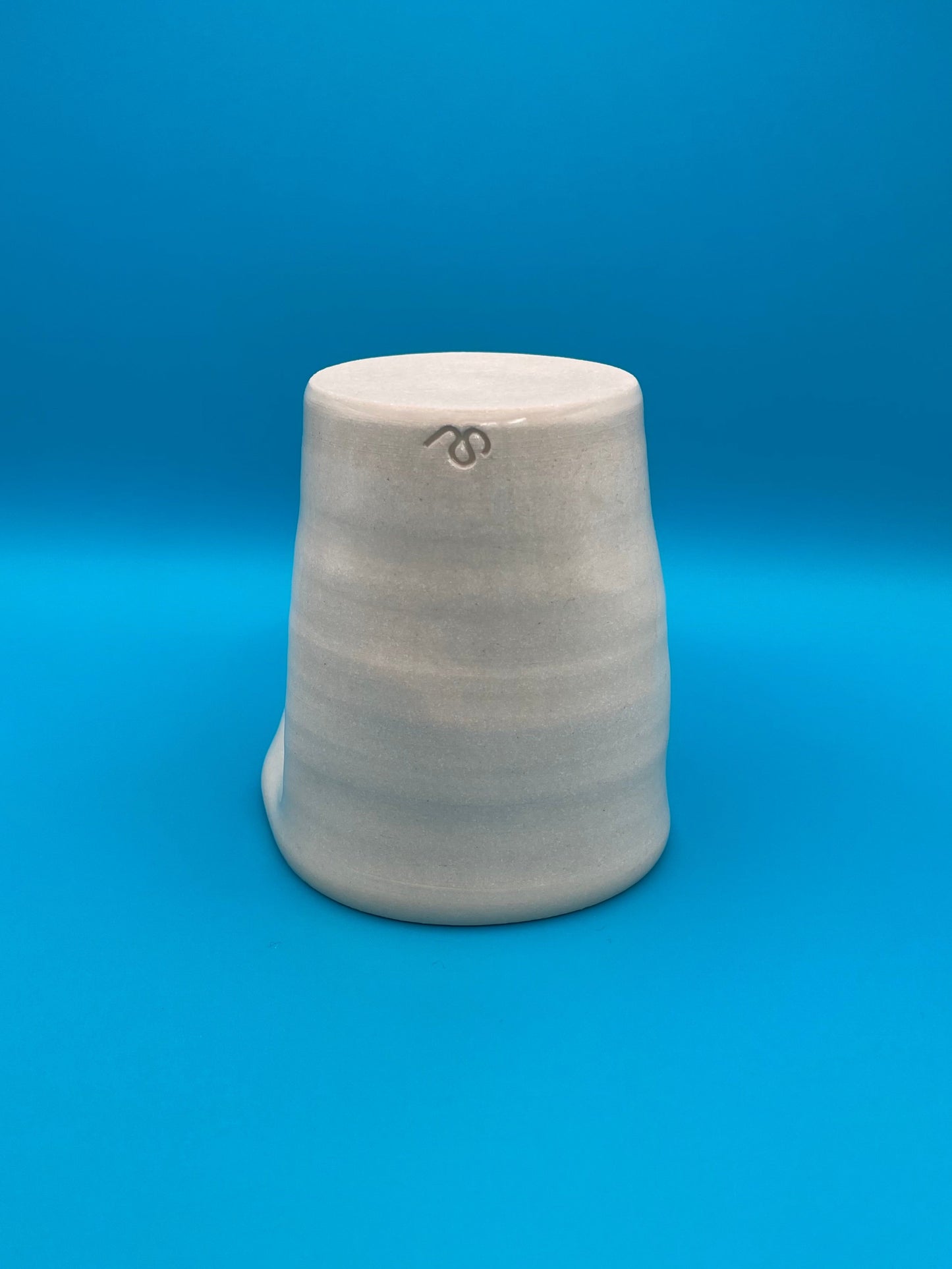 Non Paper Cup Crush – hand-thrown ceramic coffee cup with a crushed shape, made from stoneware clay and glazed with a transparent glaze, shown upside down with the S J Ceramic logo